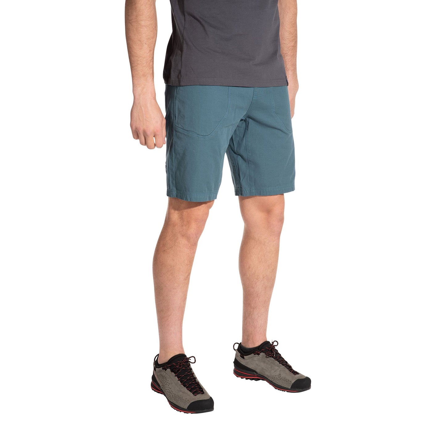 A person stands against a white background wearing a gray T-shirt, La Sportiva Flatanger Shorts Men's in teal for freedom of movement, and gray hiking shoes with black laces and red soles. The person's head is not visible in the image.