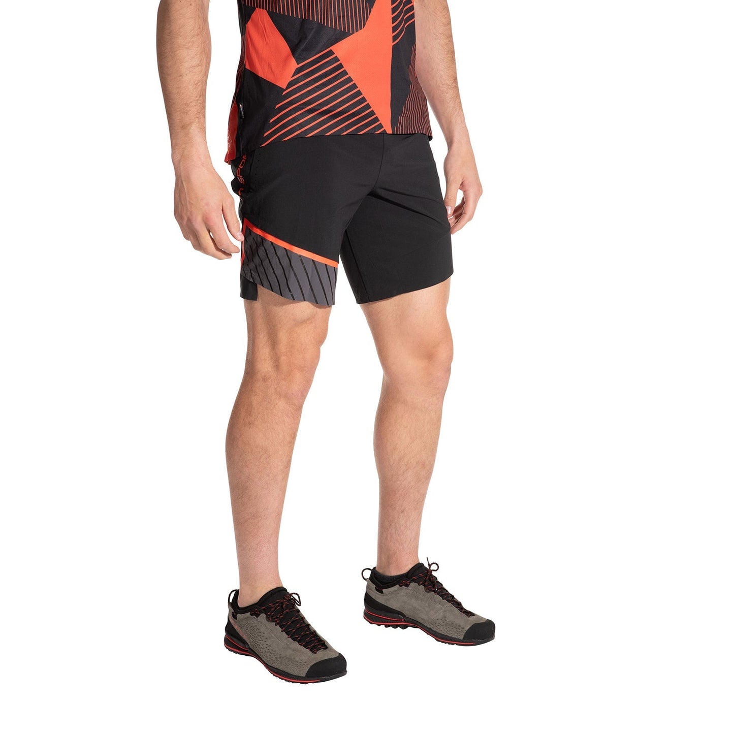 A person is shown from the shoulders down wearing La Sportiva Comp Shorts Men's (2025), featuring a lightweight black and red geometric design, paired with gray and black sneakers accented in red.