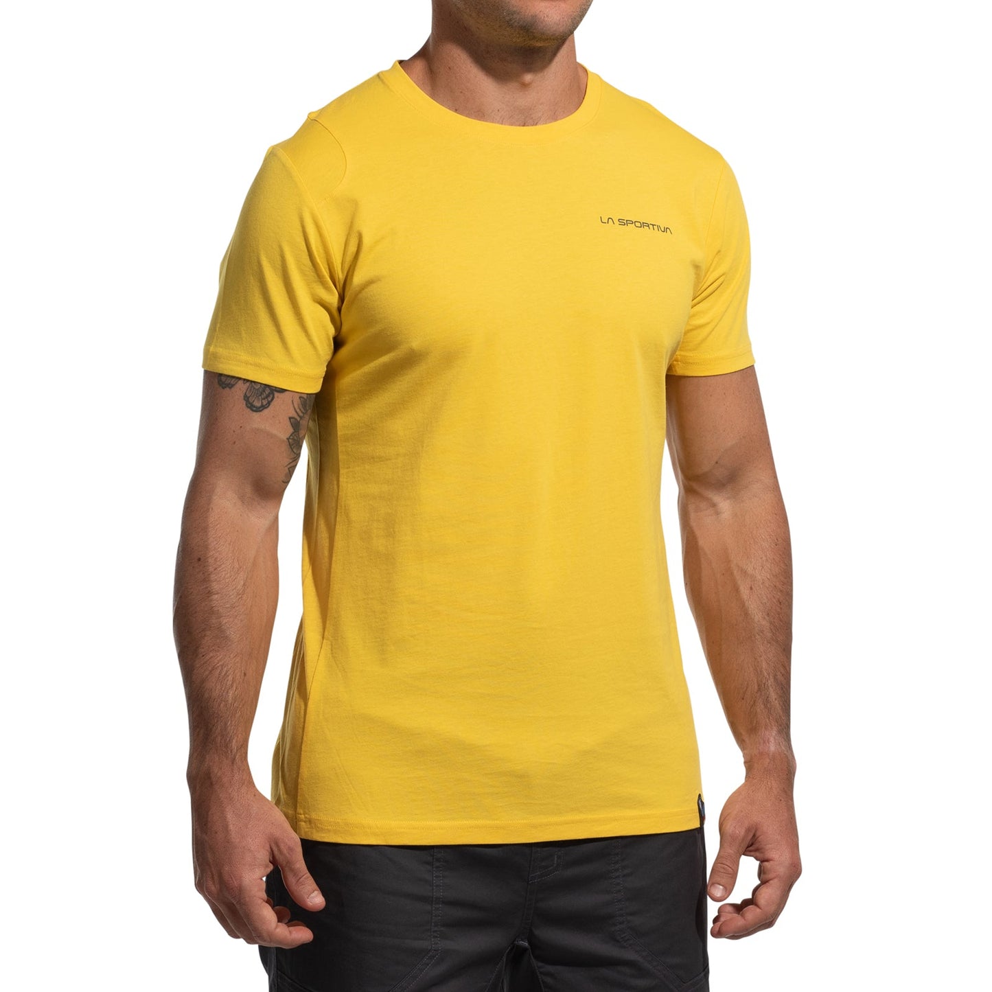 A man in a bright yellow La Sportiva Dawn Wall T-Shirt Men's with a left chest logo pairs it with black shorts. His head isn't visible, enhancing the adventurous, ascent-inspired vibe of the image.