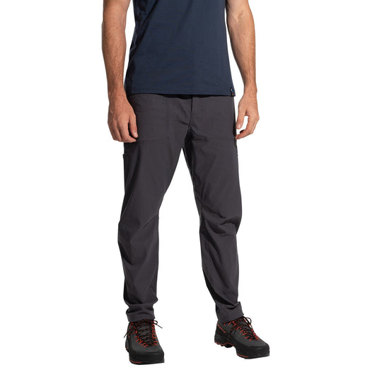 A person stands against a white background wearing a navy t-shirt, La Sportiva Talus Pants Men's (2025) in eco-friendly dark gray with articulated knees, and black hiking shoes with red laces; their face is not visible.