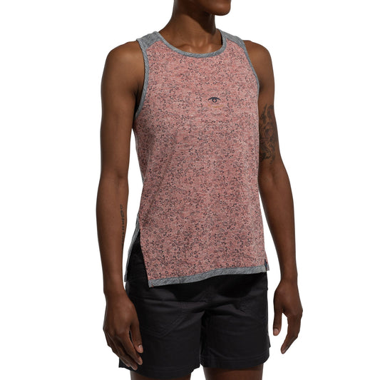 A woman wears the La Sportiva Magic Tank Women's—a sleeveless pink patterned natural fiber tank with grey trim—paired with black shorts, standing against a white background.