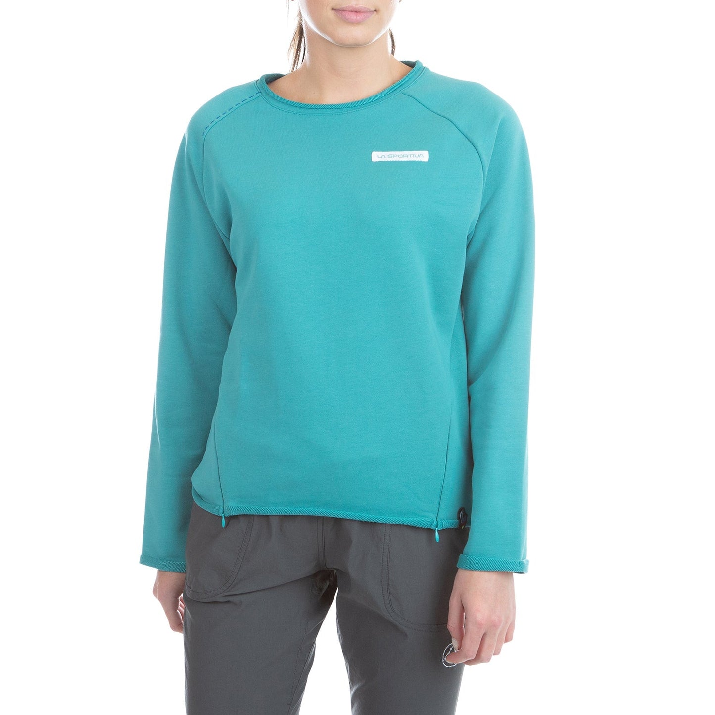 A person wearing the La Sportiva Tufa Sweater Women's (2025) in teal with dark gray pants stands against a white background, their face partially out of frame.