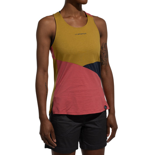 A person wears the La Sportiva Twist Tank Women's (2025) in mustard yellow, pink, and black organic cotton with the LA SPORTIVA logo on the chest, paired with black shorts, standing with arms relaxed at their sides.