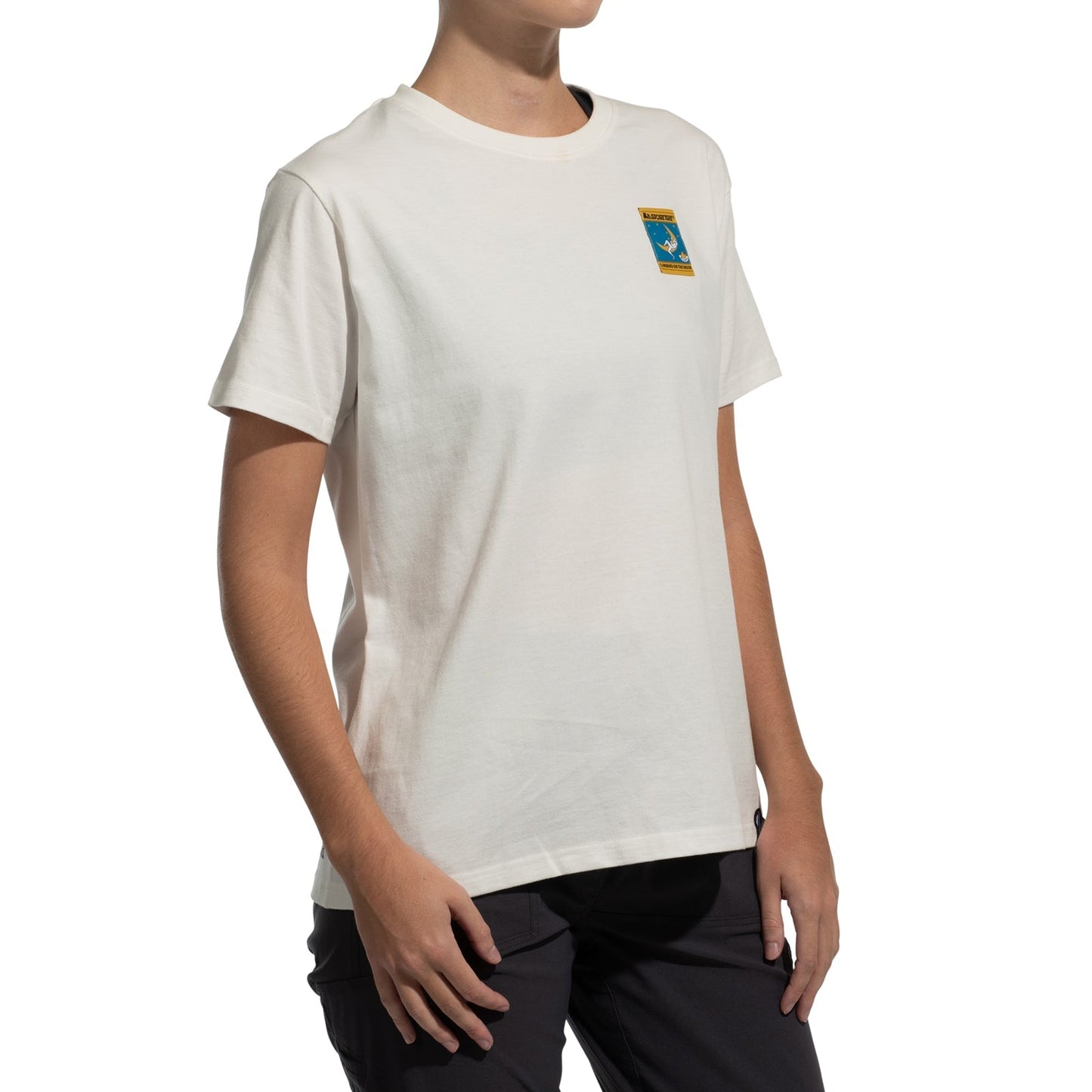 A person wears the La Sportiva Moon Climb T-Shirt Women's (2025), a white organic cotton tee with a small blue rectangle patch bordered in yellow, showing a cartoon astronaut climbing on the moon.