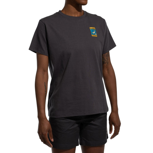 A woman wearing a La Sportiva Moon Climb T-Shirt Women's (2025), made of organic cotton with a small colorful chest patch, and black shorts stands against a white background.