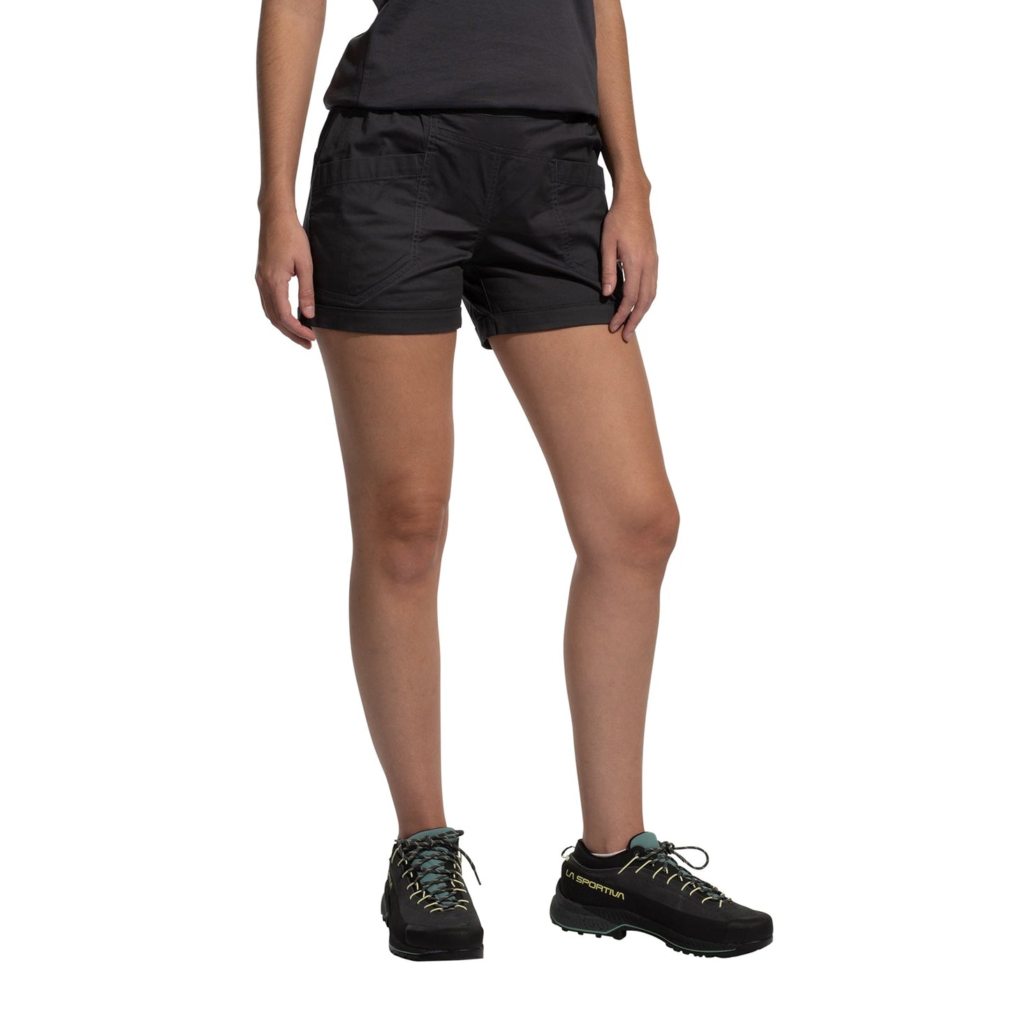 A person wearing a dark t-shirt, La Sportiva Tundra Shorts Women's with an adjustable waistband, and black hiking shoes with teal laces stands with legs slightly apart against a white background.