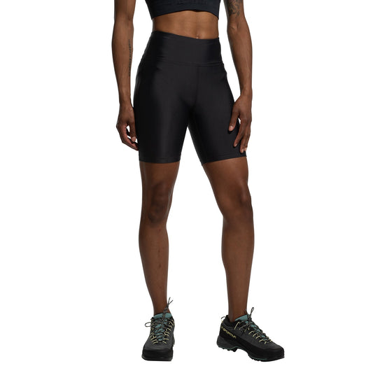 A person stands against a white background, arms relaxed, wearing a black sports bra, black La Sportiva Aerial Shorts Women's (2025) with a gusseted crotch and high waist, and black hiking shoes.