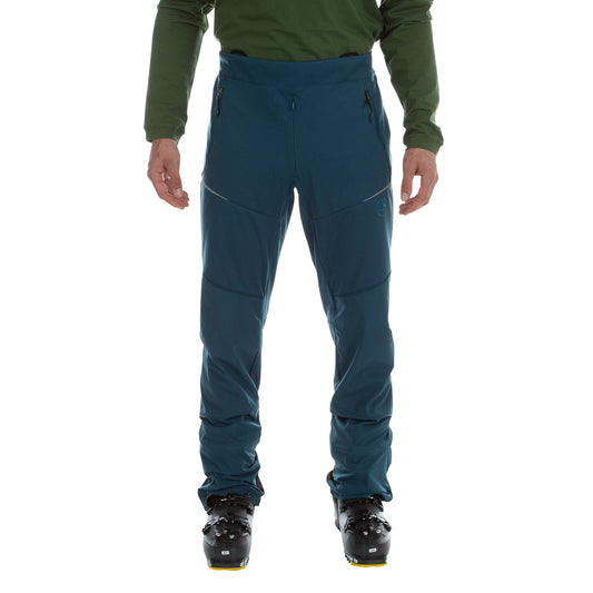 A person in a green long-sleeve shirt, La Sportiva Ikarus Pants Men's (2023), and black ski boots stands facing forward against a plain white background.