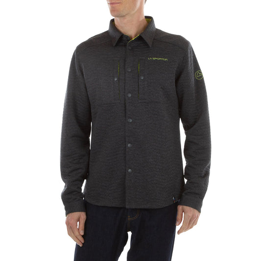 A man wearing the La Sportiva Spacer Shirt Men's in dark gray with the brand logo on chest and sleeve, featuring anti-odor technology, paired with dark jeans, stands against a white background.