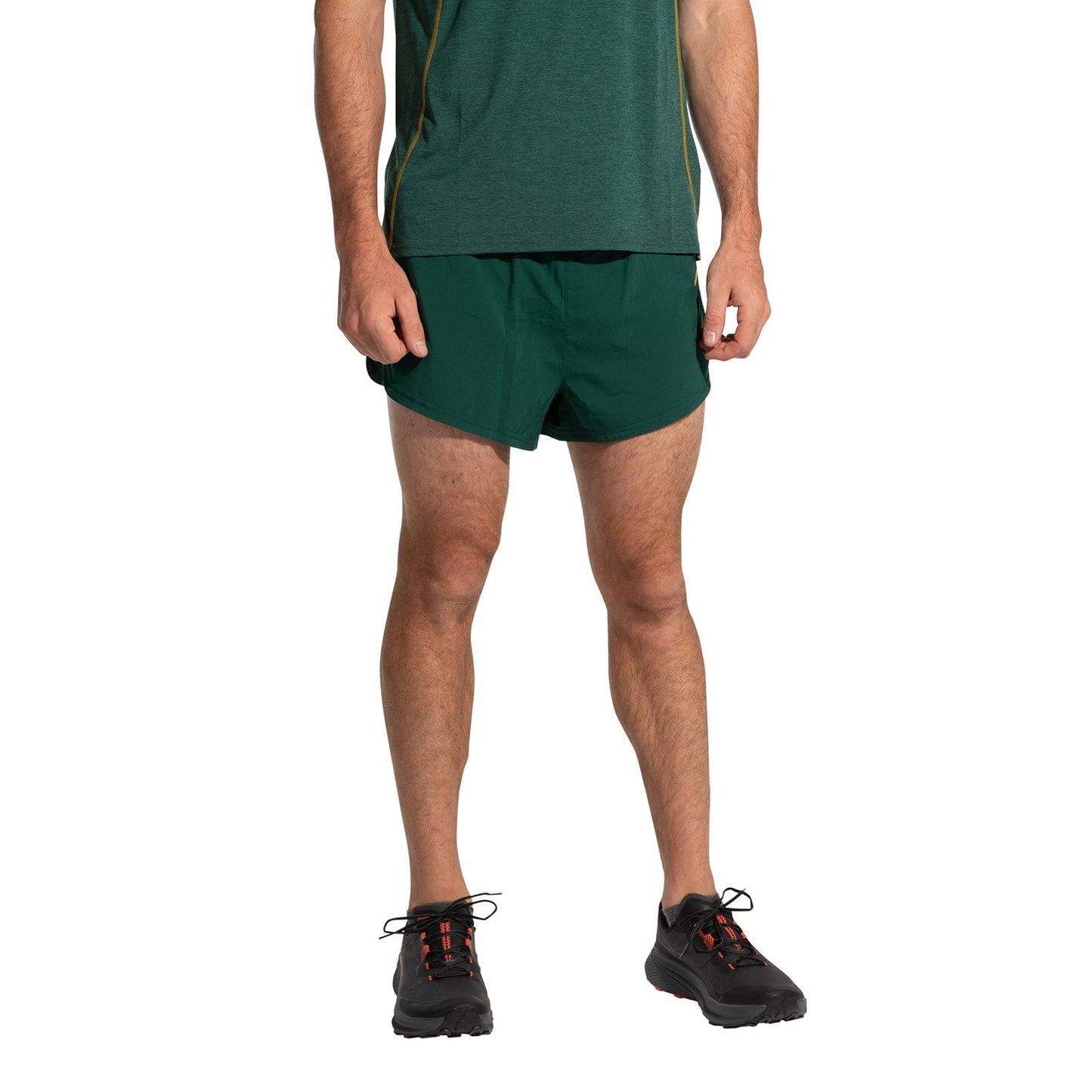 A person wears a green T-shirt, La Sportiva Auster Shorts Men's, and black running shoes with red laces, standing against a plain white background. The race-inspired look is shown without the person's head visible.