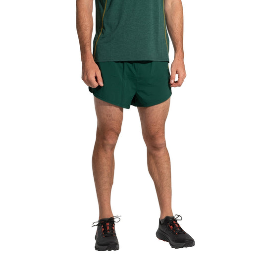 A person wears a green T-shirt, La Sportiva Auster Shorts Men's, and black running shoes with red laces, standing against a plain white background. The race-inspired look is shown without the person's head visible.