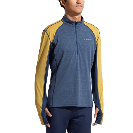 A person in the La Sportiva Swift Long Sleeve Men's shirt—blue with yellow panels, partial front zipper, and thumb holes—stands against a white background. This technical top is ideal for winter mountain running.