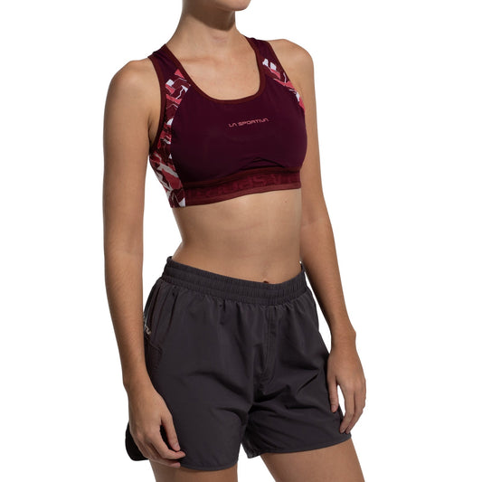 A person wears the La Sportiva Hover Top Women's in maroon with patterned straps and dark gray athletic shorts, standing with arms relaxed at their sides against a white background.