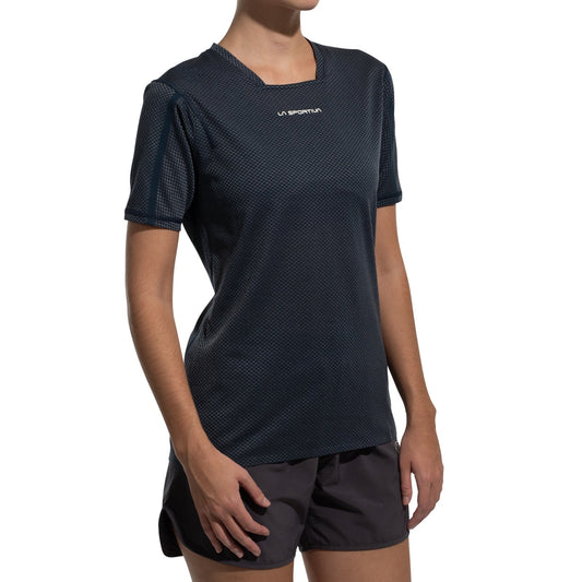 A woman models the La Sportiva Trail Bite T-Shirt Women's in a dark, ultra-lightweight fabric, paired with matching shorts. The shirt features a small white La Sportiva logo on the chest against a plain white background.