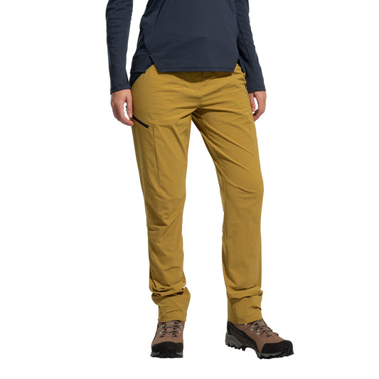 A woman wearing La Sportiva Monument Pants Women's (2025) stands against a white background, showcasing these lightweight mustard yellow hiking pants paired with brown boots and a long-sleeve navy shirt—perfect for outdoor adventure.