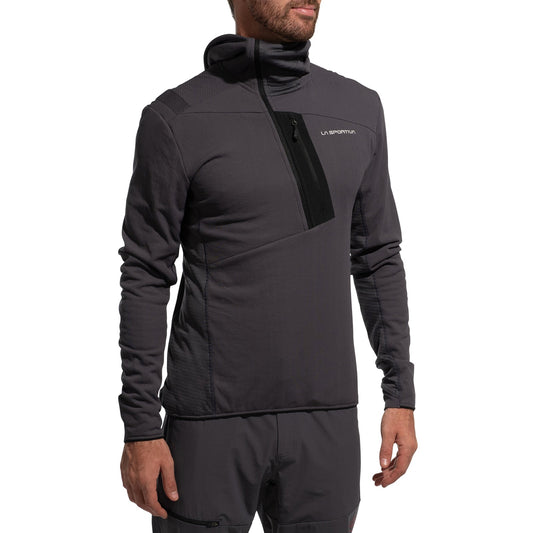 A man wears the La Sportiva Big Wall Pullover Hoody Men's (2025) in dark gray, featuring long sleeves, a high collar, chest pocket, and TechStretch Aero Fabric with Polartec inserts—paired with matching gray shorts.