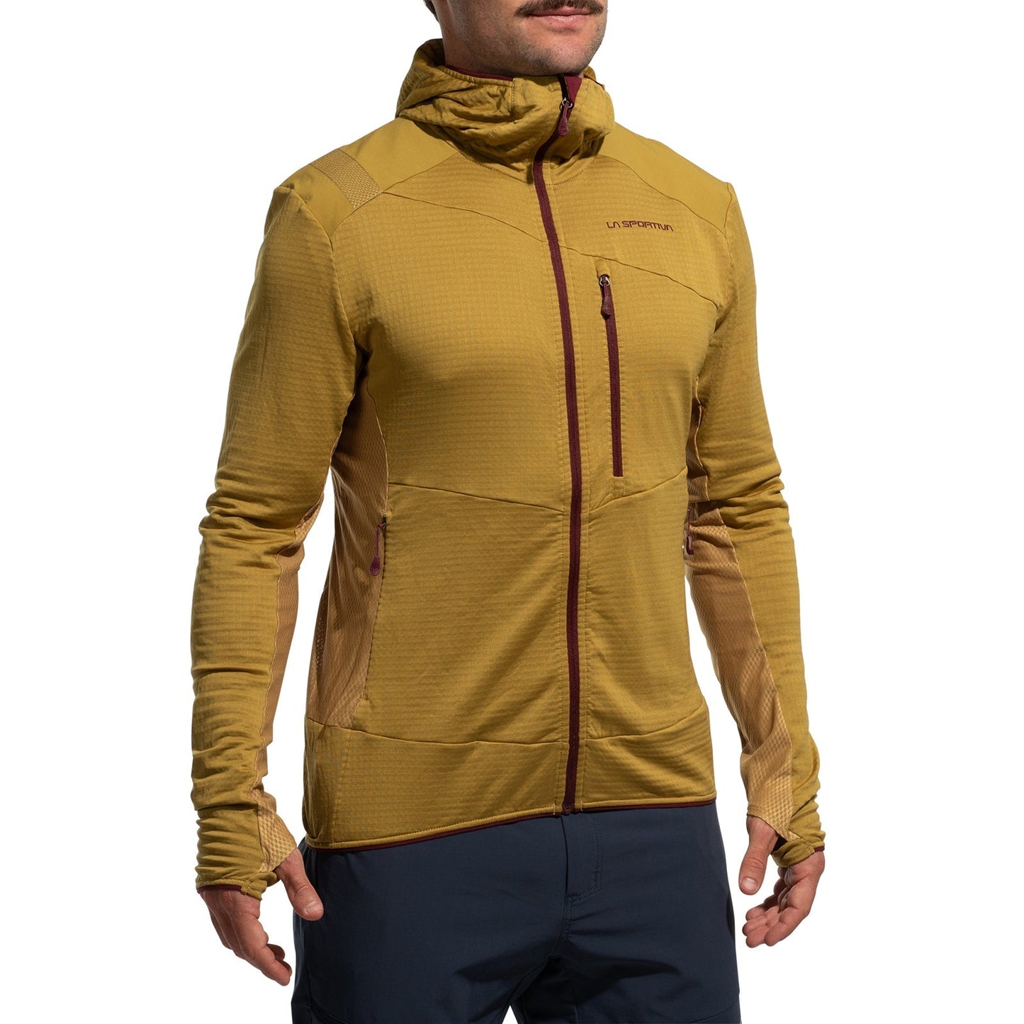 A person wears the La Sportiva Aequilibrium Thermal Hoody Men's (2025) in mustard yellow, featuring a chest zipper pocket, thumb holes, and subtle panel details, paired with dark blue pants—ideal as a fitted midlayer for outdoor adventures.