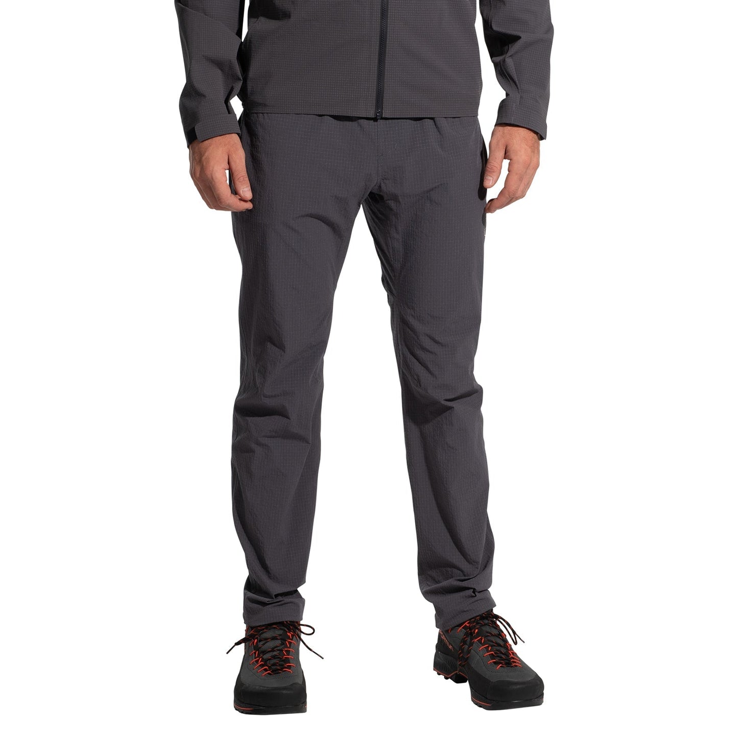 A person wearing La Sportiva Helixir Pants Men's (2025) in dark gray, featuring harness-compatible pockets, stands against a white background. The image is cropped from the shoulders down.