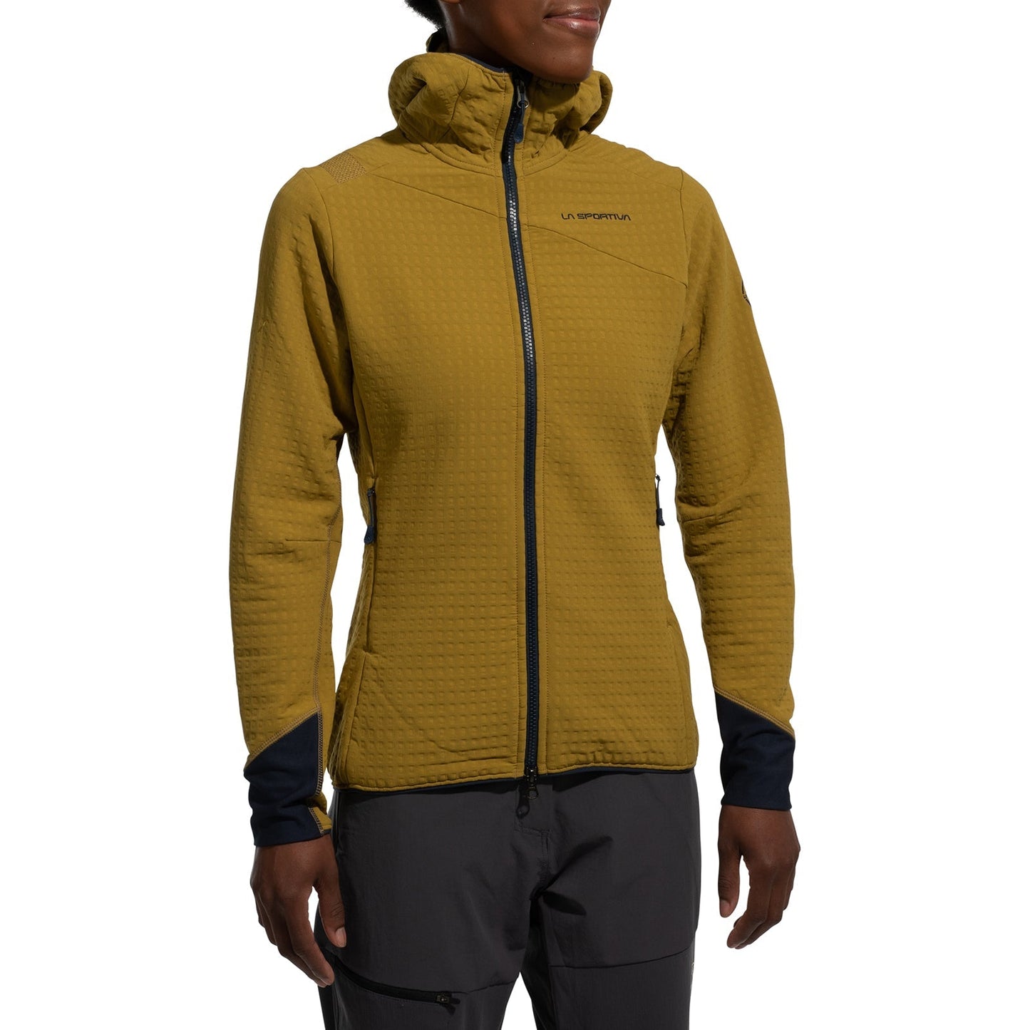 A person wears the La Sportiva Bristen Thermal Hoody Women's in mustard yellow, a textured, hooded fleece with zippered front and pockets, plus black trimmed cuffs—ideal for outdoor activities—paired with gray pants. The face is partially out of frame.