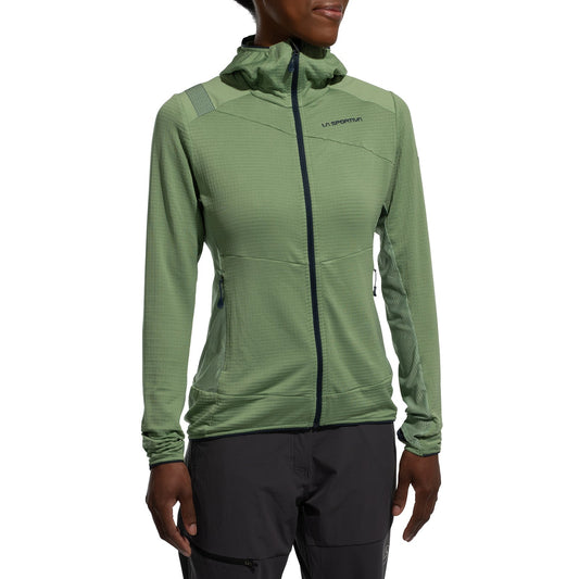 A woman wears the La Sportiva Aequilibrium Thermal Hoody Women's (2025) in light green, featuring a chest logo and dark gray pants as a mountaineering mid-layer, standing against a plain white background.