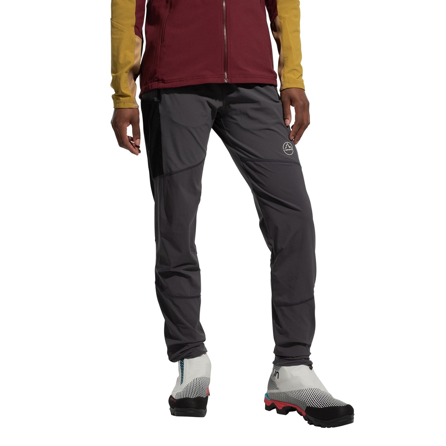 A person in a maroon and yellow jacket, La Sportiva Aequilibrium Speed Tights Women's (abrasion-resistant gray), and white trail running shoes with black and red soles stands against a plain white background.