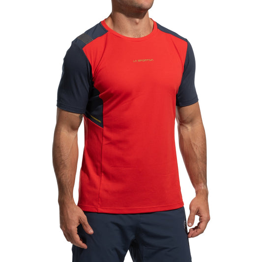 A man wears the La Sportiva Ridge T-Shirt Men's (2025) in red with dark navy sleeves and navy shorts. The moisture-wicking tee features Polartec Delta Cooling Fabric and "La Sportiva" branding on the chest, set against a white background.