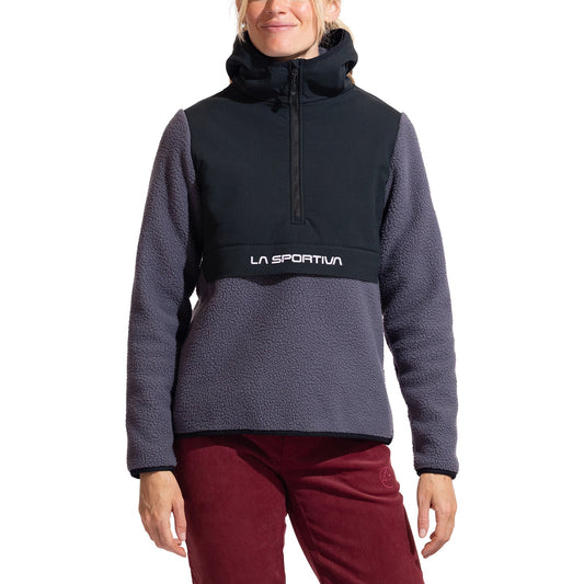 A person wears the La Sportiva Guidance Sherpa Hoody Women's, featuring a color-block design with a black upper, purple lower section, front zip, hood, and logo across the chest, paired with maroon pants.
