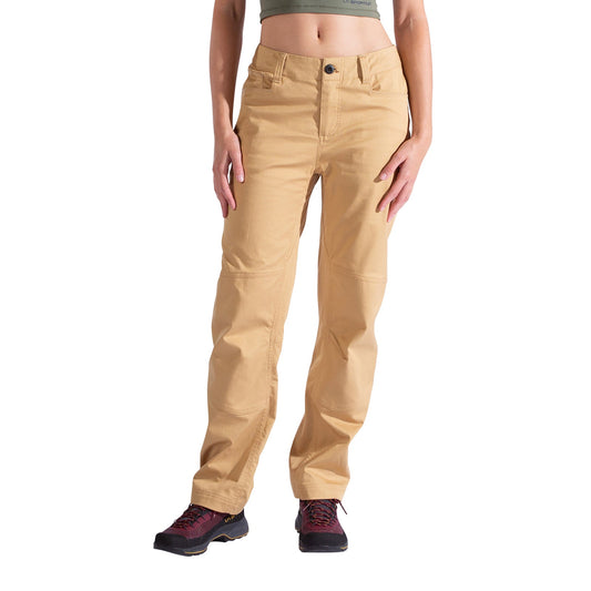Wearing La Sportiva Mainliner Pants Women's in tan, a cropped olive green top, and black hiking shoes with red laces, the person stands against a white background with their arms relaxed at their sides.