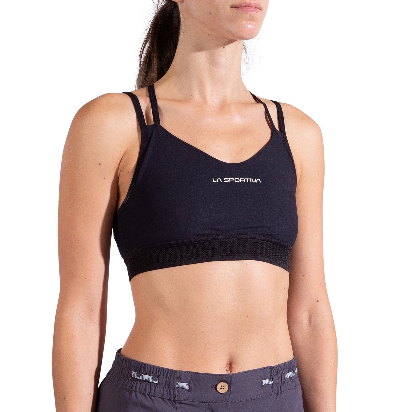 A woman wearing the La Sportiva Boulder Bra Women's in black and gray athletic pants stands against a white background, with "La Sportiva" printed on the front of the sports bra.