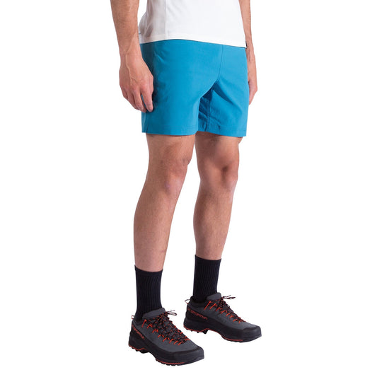 A person stands against a plain white background, cropped below the shoulders, wearing La Sportiva Gambit Shorts Men's in bright blue, a white shirt, black socks, and black hiking shoes with red laces.