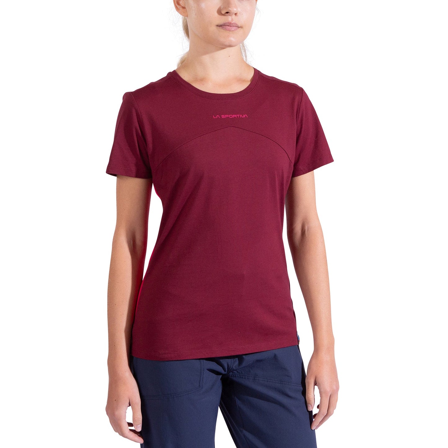 A woman in a short-sleeved, burgundy La Sportiva Roof T-Shirt (organic cotton) and dark blue pants stands against a plain white background. Her face is partially visible, with her hair tied back.