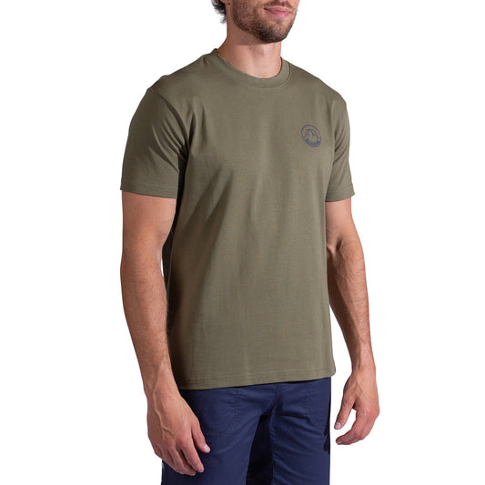 A man wearing the La Sportiva Circle Logo T-Shirt Men's in olive green, featuring a small circular logo on the left chest, and dark blue pants stands against a white background.