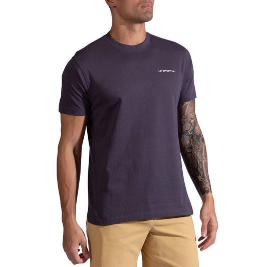 A man sports the La Sportiva Trilogy T-Shirt Men's, a dark purple heavyweight organic cotton tee with small white logo on the chest, paired with light beige shorts and a tattoo sleeve—ideal attire for exploring Boulder's Flatirons.