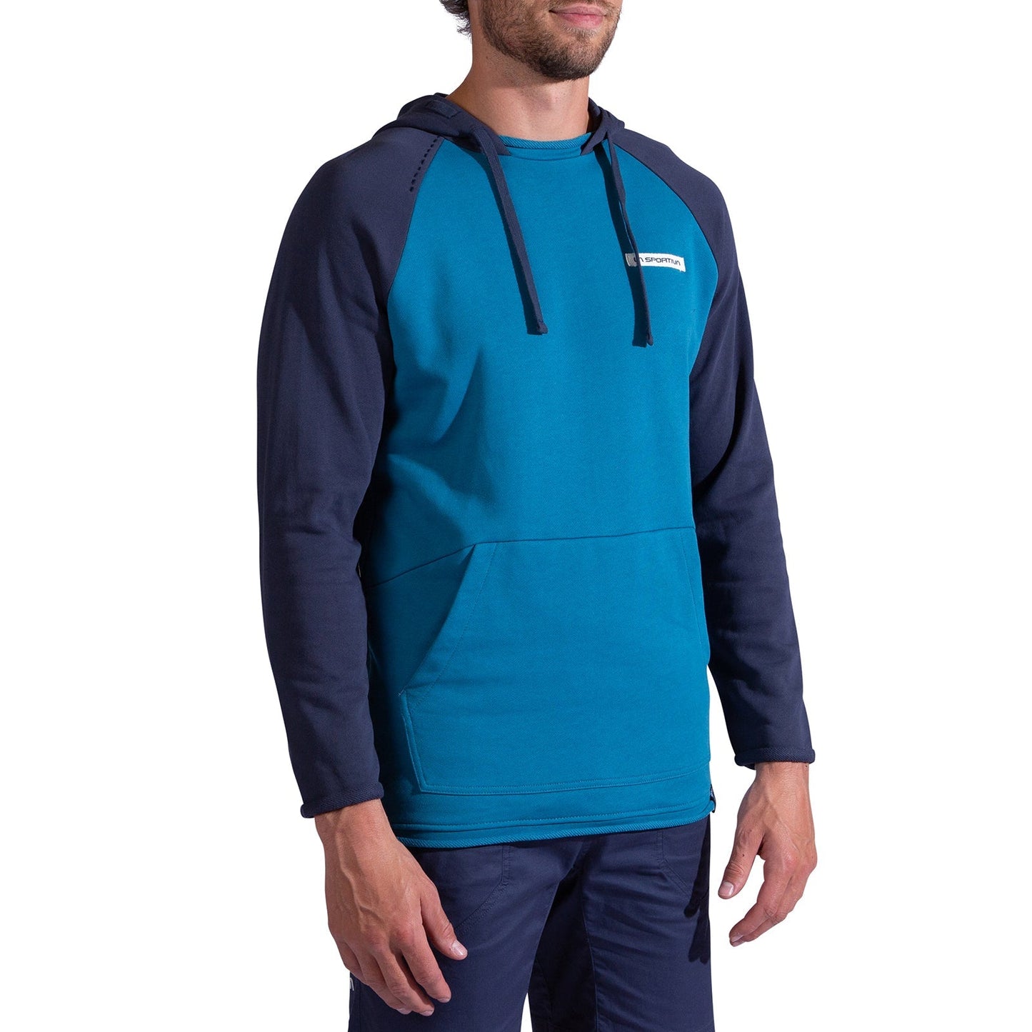 A man wears the La Sportiva Telendos Hoody Men's in teal and navy, featuring a front pocket, navy sleeves, a small white chest logo, and made from organic cotton. He pairs it with matching navy blue pants.
