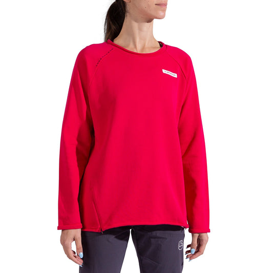 A woman models the La Sportiva Tufa Sweater Women's in vibrant pink with dark pants, standing against a plain white background, her hair tied back and head slightly turned to the side.