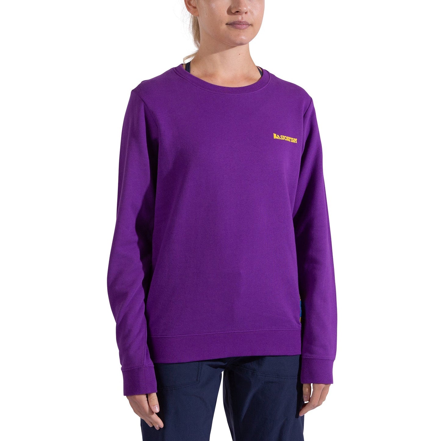 A woman in a bright purple La Sportiva Climbing on the Moon Sweatshirt Women's with a small yellow logo on the chest and dark pants stands against a plain white background. Her face is partially visible.