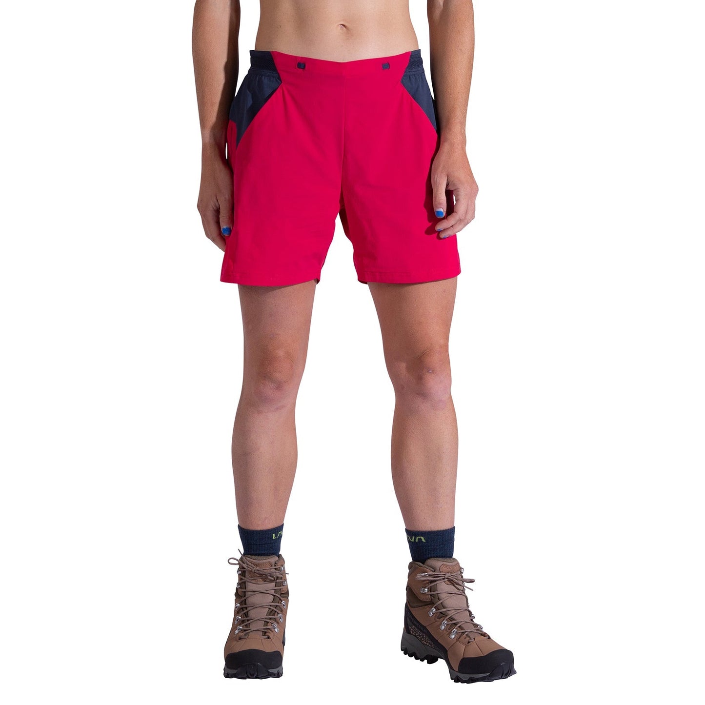 A woman wears La Sportiva Trail Guard Shorts with dark side panels, blue socks, and brown hiking boots, ideal for fast-hiking, standing relaxed against a white background.