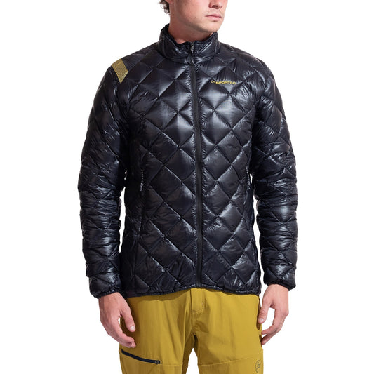 A man wears a shiny black La Sportiva Lumina 100 Down Jacket with lightweight insulation, high collar, and subtle chest logo, paired with yellow outdoor pants. He stands facing forward, hands relaxed by his sides.