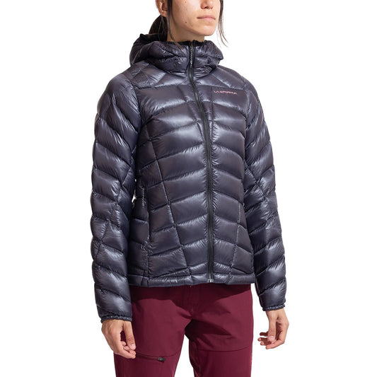 A woman wears the La Sportiva Lumina 200 Down Jacket—a shiny, dark gray, lightweight, hooded down jacket—paired with maroon pants, standing against a plain white background.