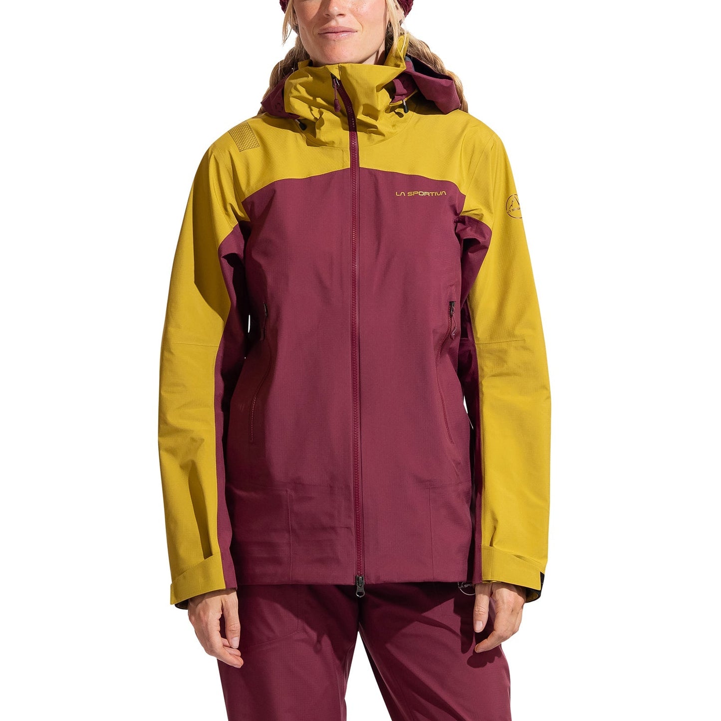 A woman faces forward against a white background, wearing the La Sportiva Alpine Guide GTX Performance Jacket with a maroon body and yellow shoulders, sleeves, and hood—designed for alpine activities.