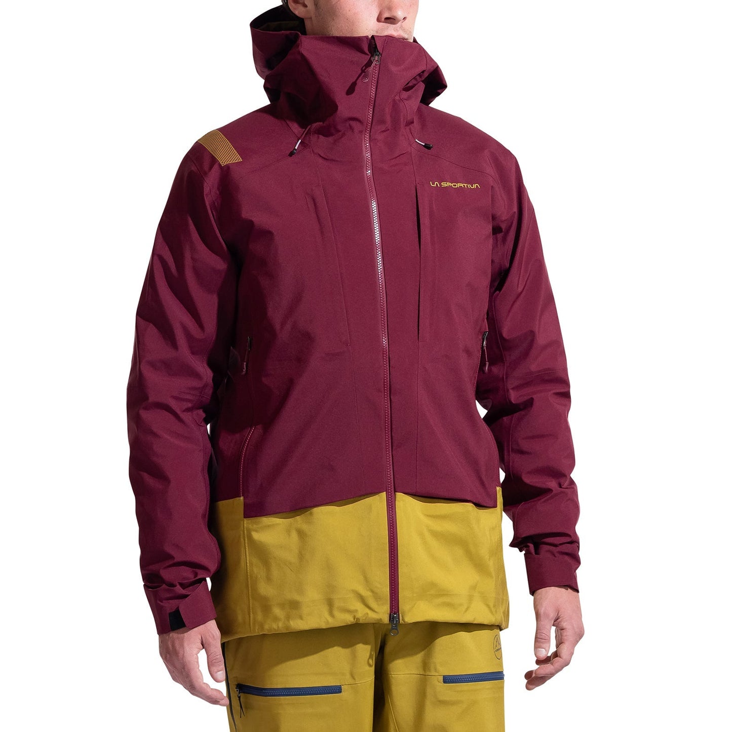A person wearing the La Sportiva Sender GTX Performance Jacket Men's with a maroon upper and mustard yellow lower, featuring a hood, front zipper, chest pocket, and matching mustard yellow pants—ideal for ski touring.