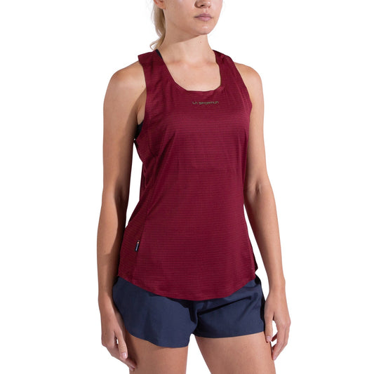 A woman wearing a La Sportiva Pure Tank Women's quick-drying sleeveless maroon top and navy blue shorts stands against a plain white background.