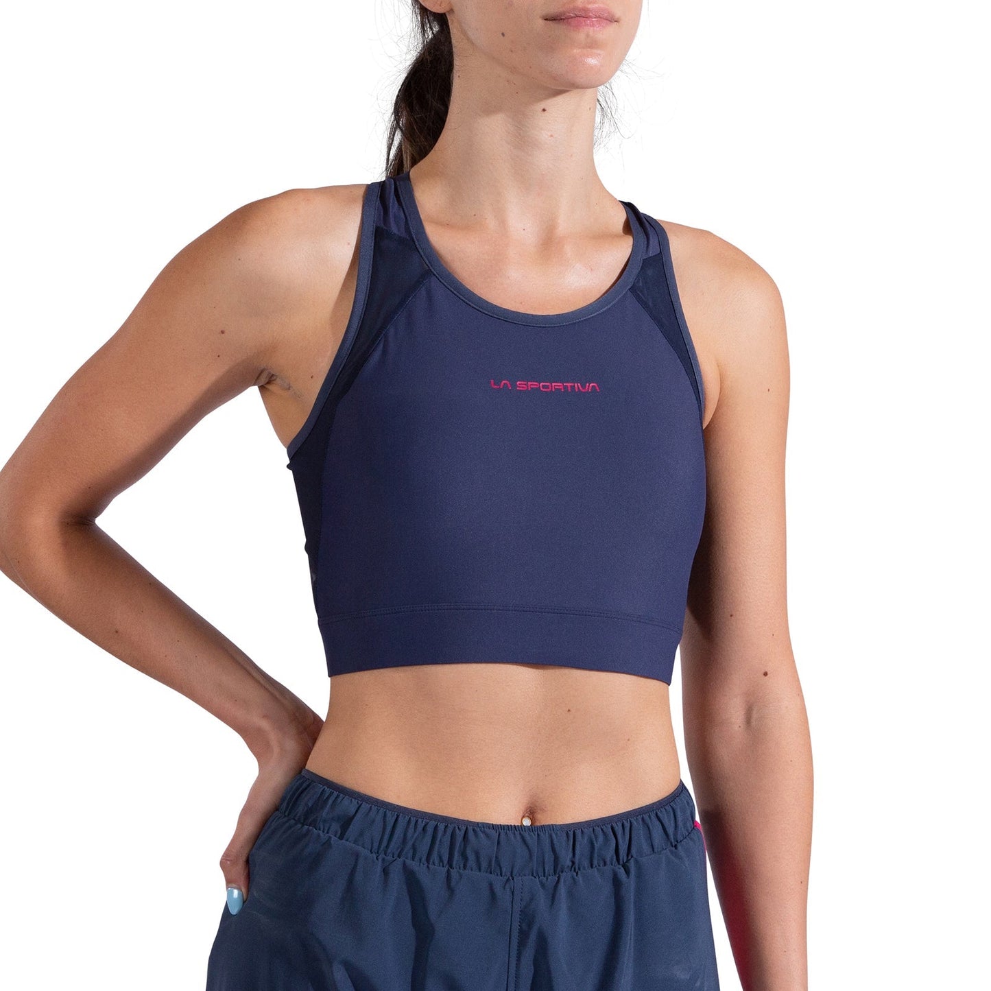 A woman models the La Sportiva Stash Bra Women's and matching shorts in navy blue, standing against a white background—ideal medium-support for trail runs.