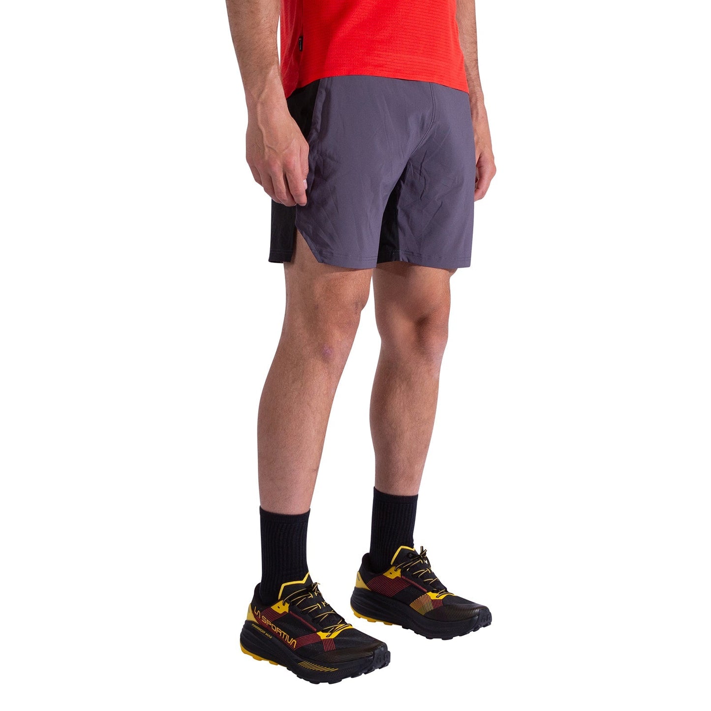 A person in a red shirt, La Sportiva Pure 7 Inch Shorts Men's (gray), black socks, and black and yellow running shoes stands against a plain white background.