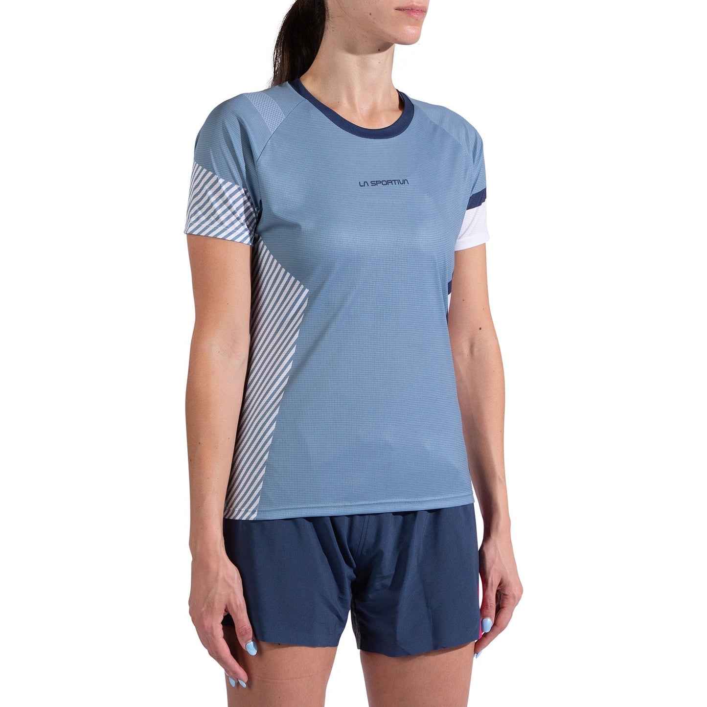 A woman wears the La Sportiva Flow T-Shirt Women's in light blue with white and striped accents, paired with dark blue shorts. She stands against a plain white background, with her face partially out of frame.