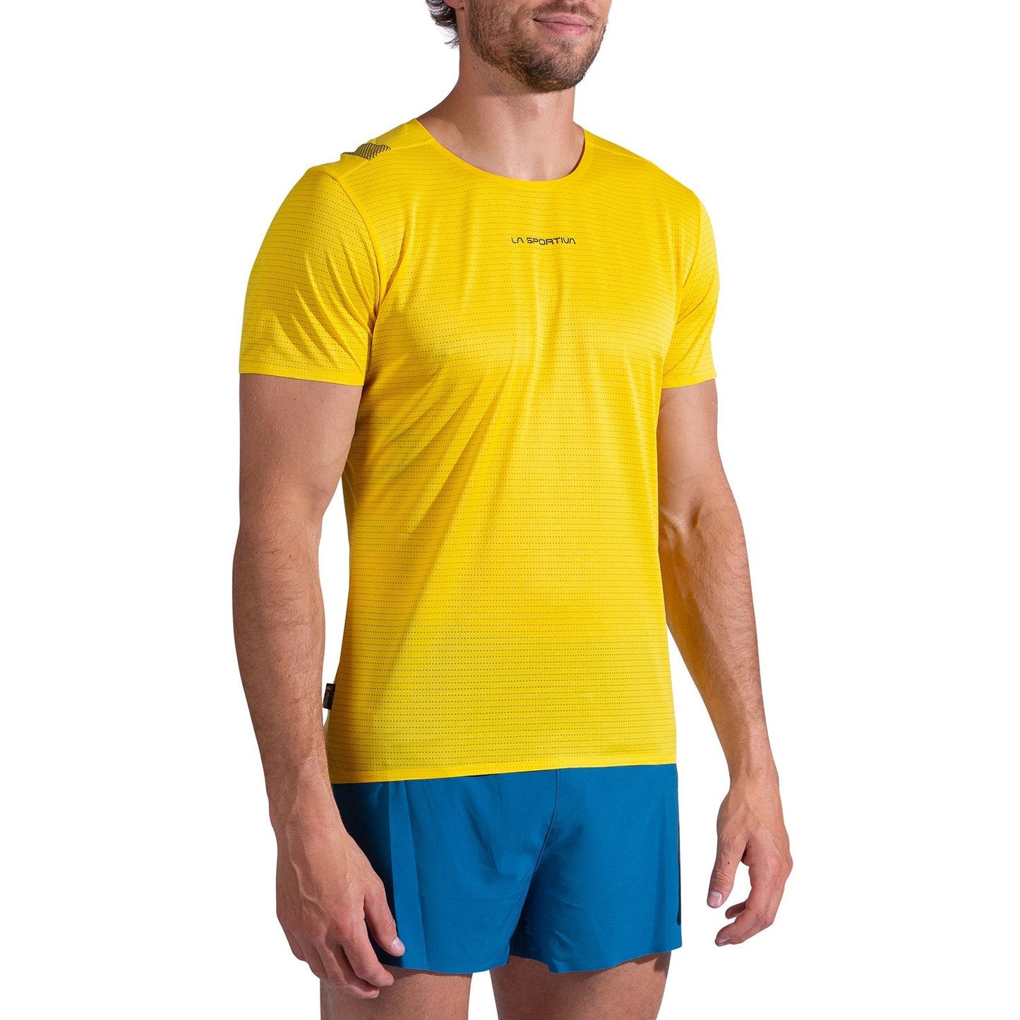 A man wears the La Sportiva Pure T-Shirt Men's in bright yellow recycled polyester with blue shorts, standing against a white background and facing slightly to the side.