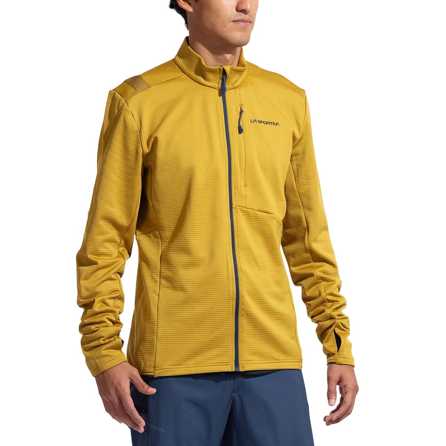 A person wears the La Sportiva Chill Thermal Jacket Men's in mustard yellow, featuring a full zip, high collar, and chest pocket, paired with blue pants, standing against a plain white background.