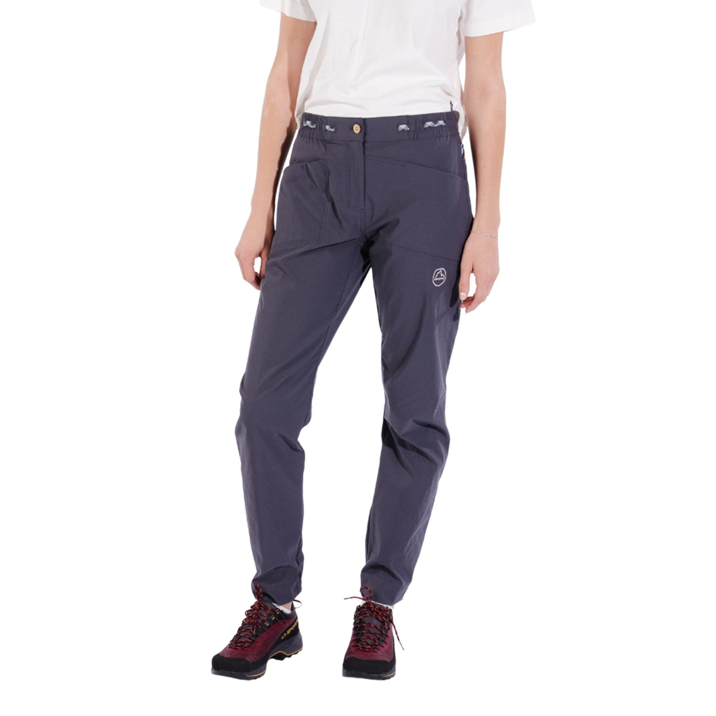 A person wears a white short-sleeve T-shirt, La Sportiva Mantra Pants Women's in dark gray with articulated knees, and maroon hiking boots, standing against a plain white background. Their head is out of the frame.