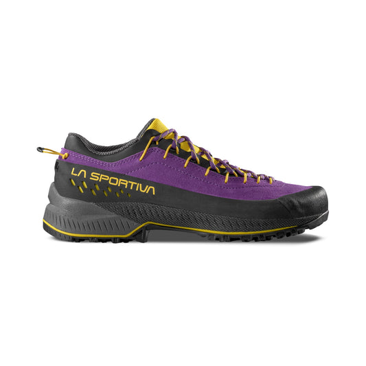A side view shows the La Sportiva TX4 EVO Women's hiking shoe in purple, black, and yellow, highlighting its rugged Vibram Megagrip sole, laces, and LA SPORTIVA branding for maximum stability.
