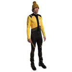 A man wears the La Sportiva Stratos VI Racing Suit Men's in yellow and black, paired with black ski boots and a yellow pom-pom knit hat, standing against a white background.